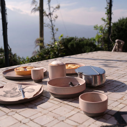 Moodbild. Simple aber schön arrangierter Frühstückstisch auf einer italienischen Terrasse mit Blick auf See und Berge in der Ferne, zwei Krostate (typischer, italienischer Kuchen) serviert auf dem Lietzensee Dinnerteller und Pastateller in altrosa mit einem Capuccino und einem Espresso macchiato in Lietzensee Becher und Tasse in altrosa.