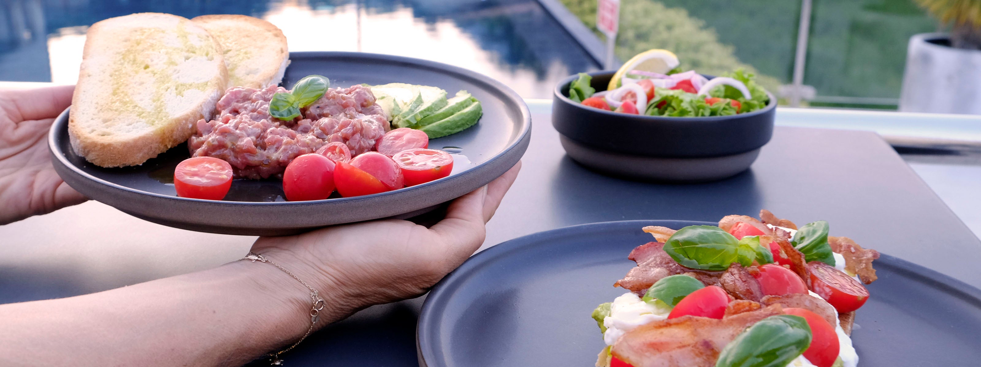 schwarzes Steinzeugkeramik Geschirrset am Pool gedeckt mit Bruschetta und Beef Tartar