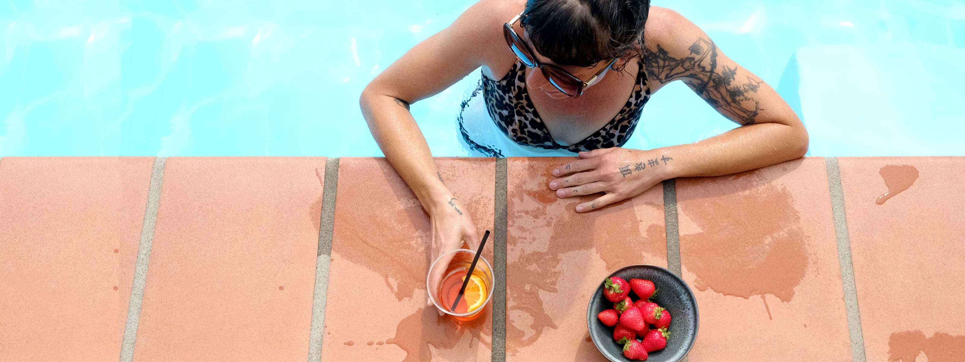 Frau im Bikini genießt einen Aperitivo mit einer hangemachten Keramikschale voller frischer Erdbeeren im Pool.