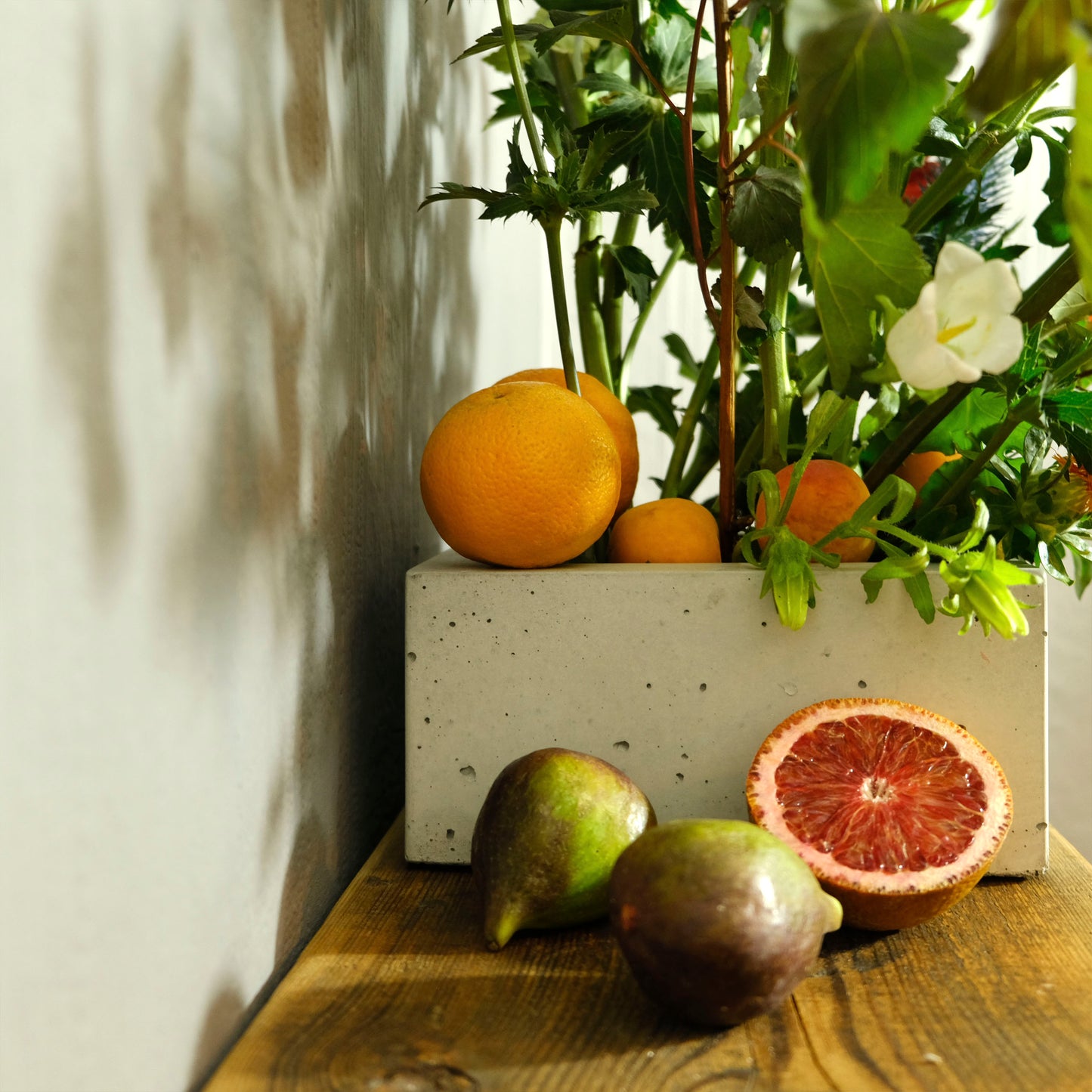 Pflanzgefäß BLOCK aus hellgrauem Beton mit Blumengesteck und Feigen und Orangen